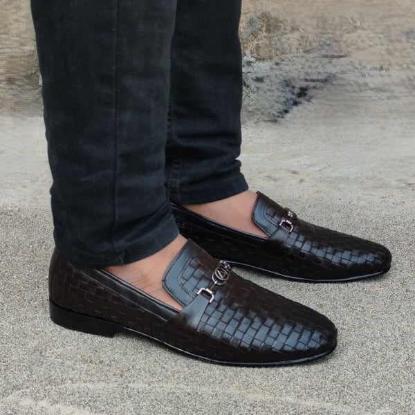 Black leather loafers worn with dark pants against a textured wall.