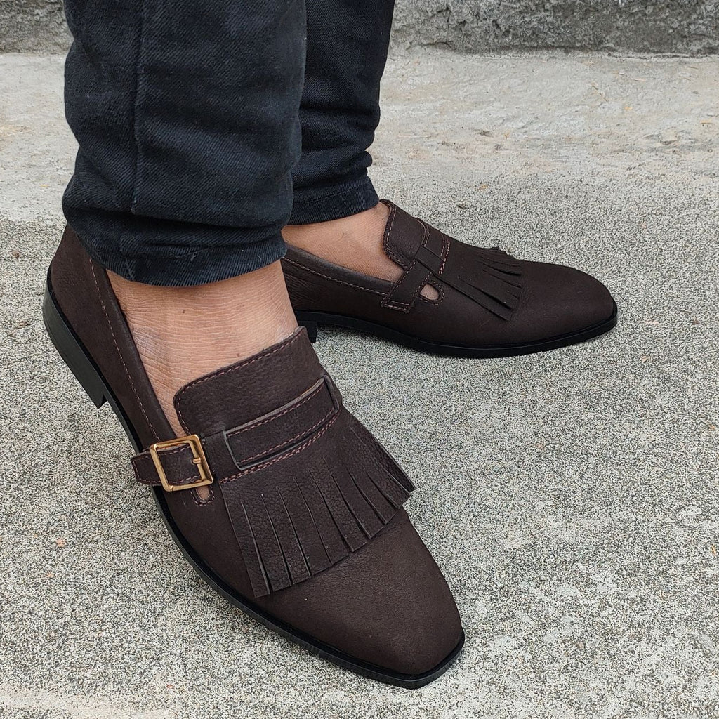Brown loafers with fringes worn by a person on a concrete surface.