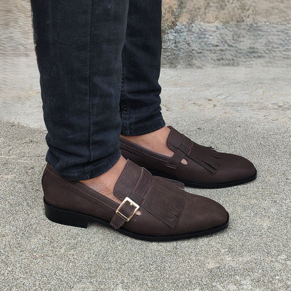 Brown loafers worn with dark jeans on a concrete surface.