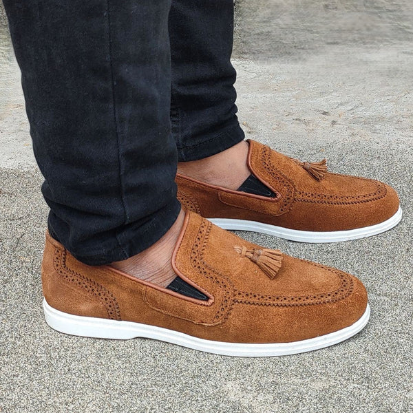 Brown loafers worn with black pants on a concrete floor.