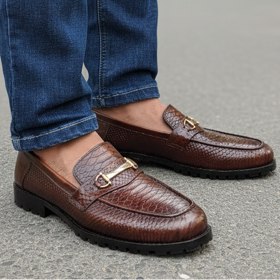Brown leather loafers worn with blue jeans on a blurred outdoor background