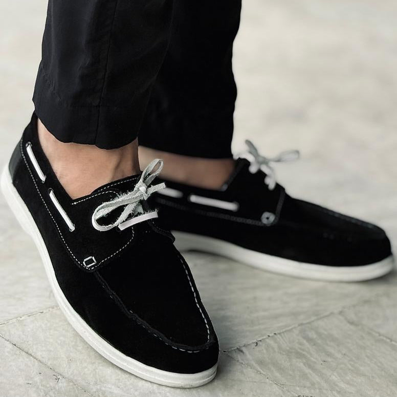 Black casual shoes worn with black pants on a light wooden floor.