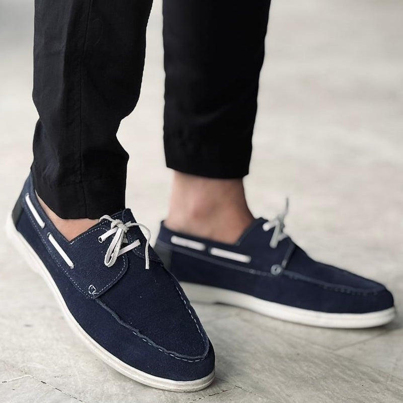 Navy blue casual shoes worn with black pants on a light gray pavement.